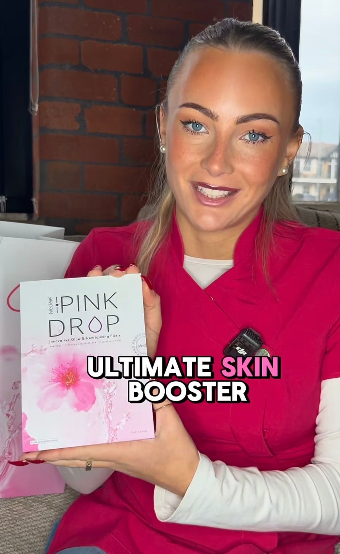 Woman holding a product box labeled 'The Pink Drop Ultimate Skin Booster' in an indoor setting.