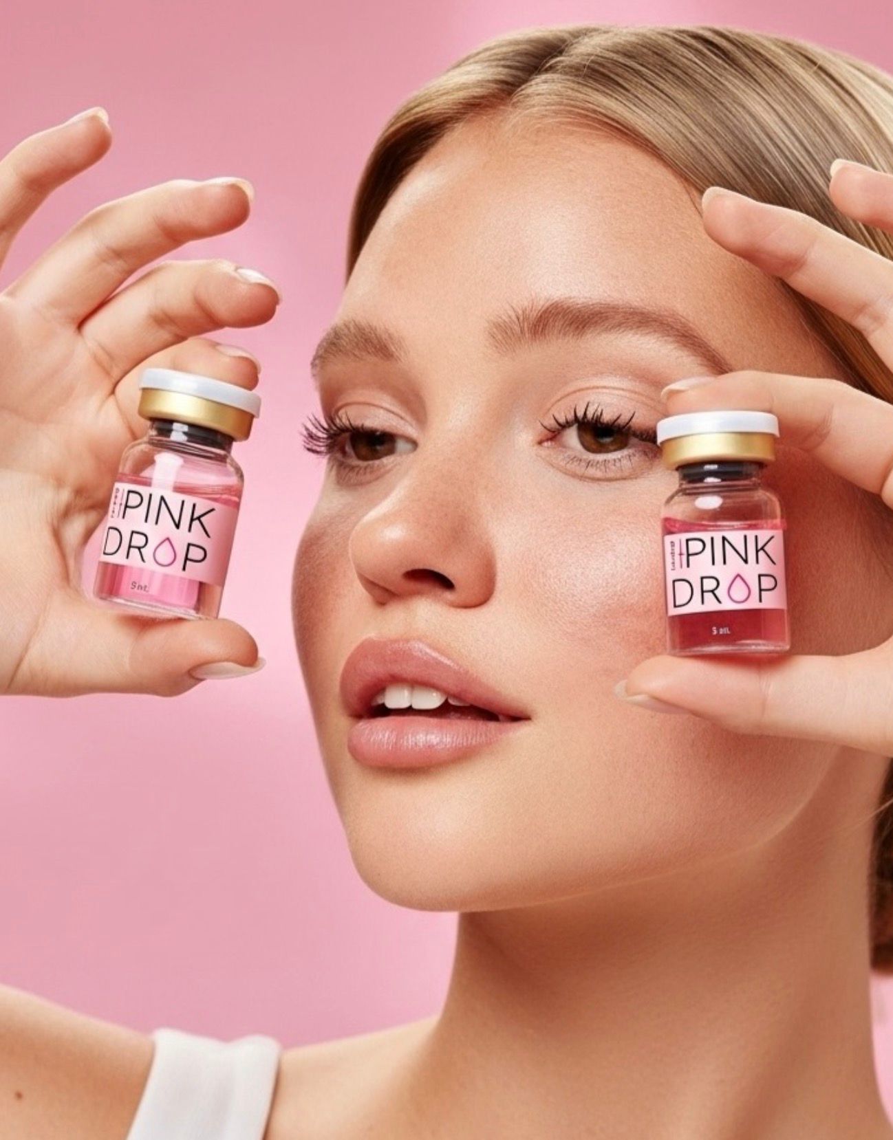 Woman holding 'Pink Drop' skincare products against a pink background