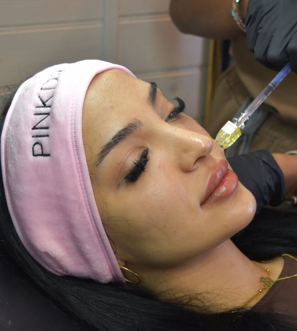 Person receiving a facial treatment with a pink headband in a clinical setting.